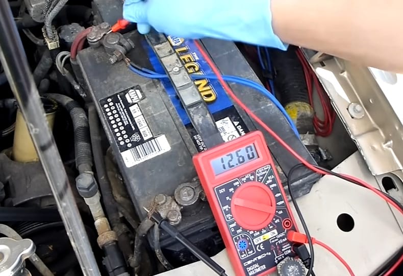 A person connecting the lead probe of a multimeter to car batter