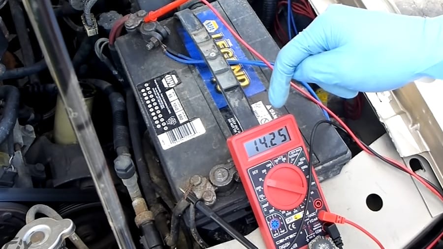 A person is using a multimeter to test a car battery; the multimeter at 14.25 reading