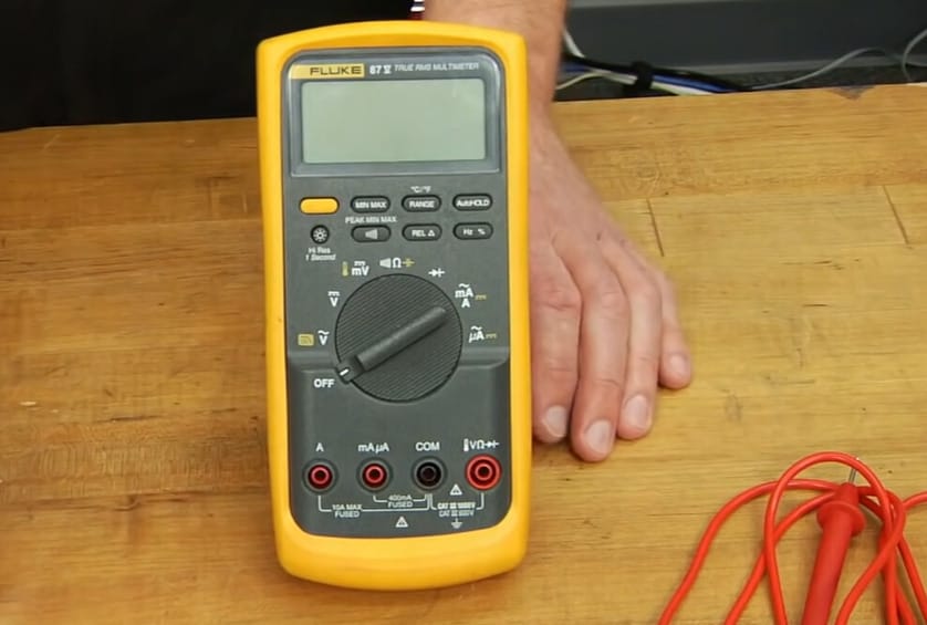 A person holding a multimeter in a wooden table