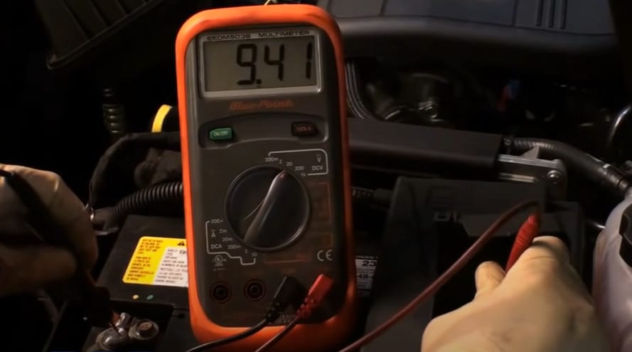 A person is using a multimeter to check the battery in a car