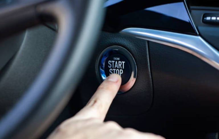 A person activating the start button on a car