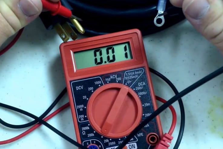 A person is holding a Centech multimeter with wires attached to it
