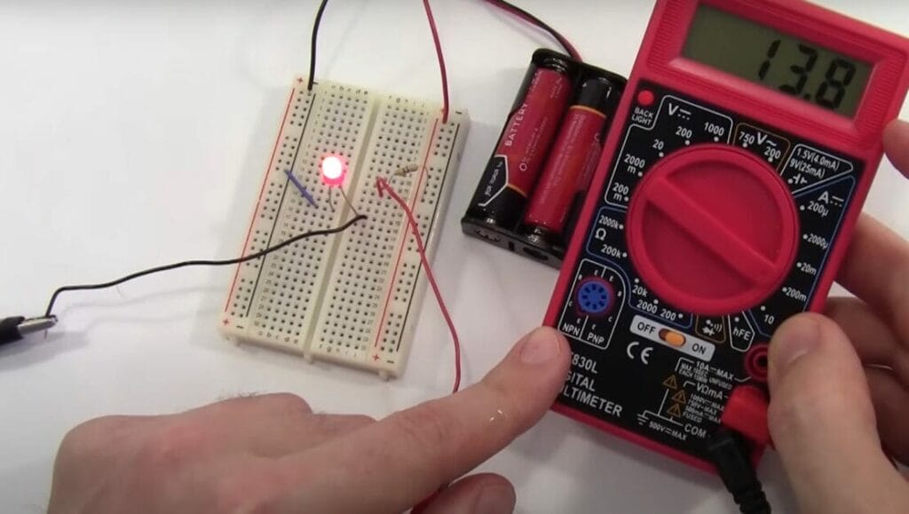 A person is using a Cen Tech multimeter to test a circuit board and batteries
