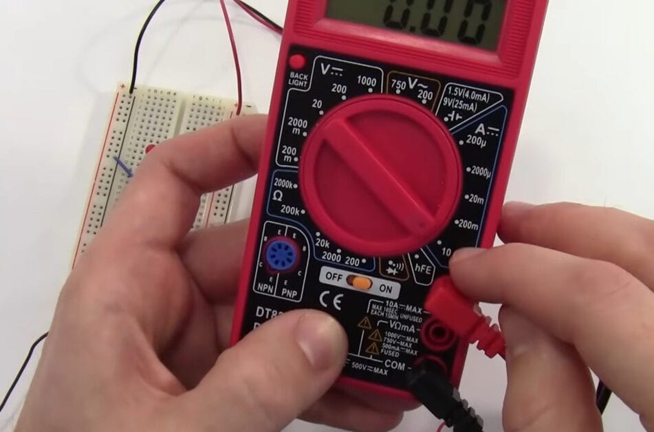 A person is using a red Cen Tech multimeter to test a circuit