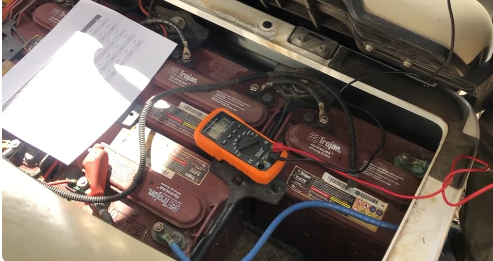 A car battery with a multimeter attached to it, measuring its voltage
