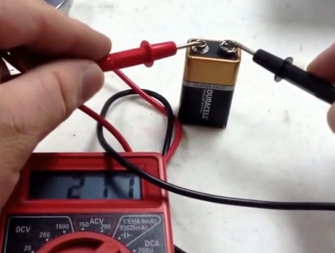 A person is using a Centech multimeter to test a battery