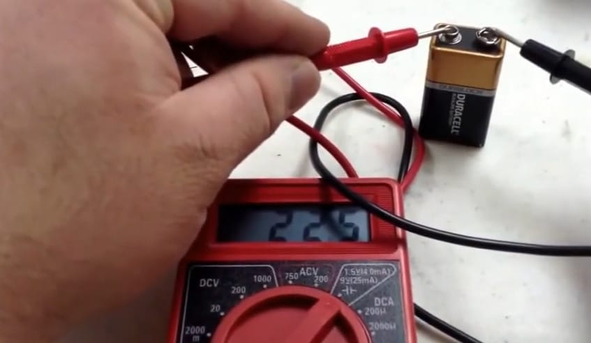 A person is using a cen tech multimeter to test a duracell battery