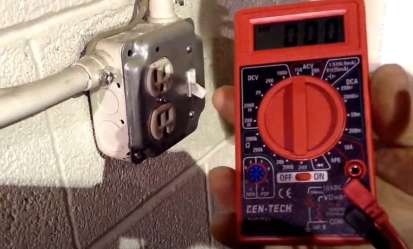 A Cen Tech multimeter being held next to a wall outlet