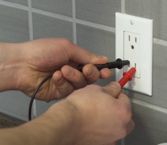 A person is using a multimeter to check an outlet