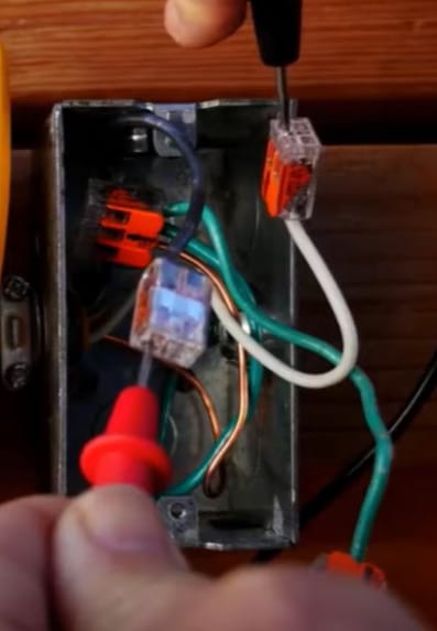 A person is using a multimeter to check an outlet's voltage