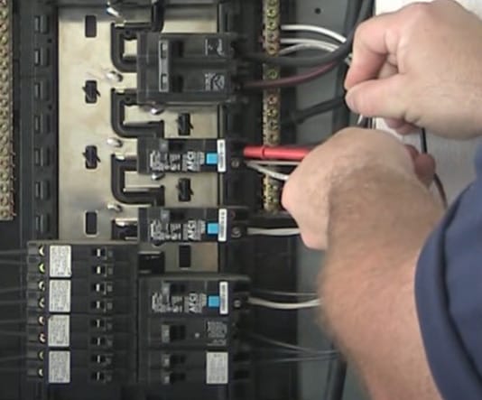 A man is carefully testing a circuit breaker with a multimeter