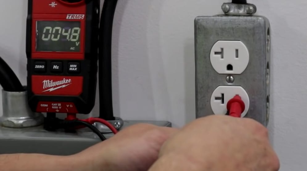 A person inserting the red probe of as voltmeter into an outlet