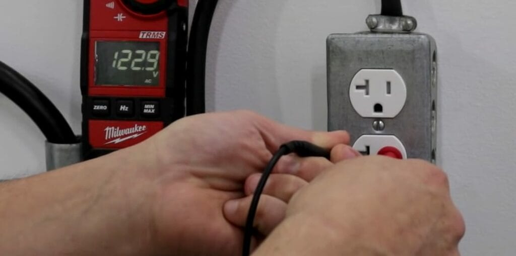 A person inserting the voltmeter's lead probe into the wall outlet