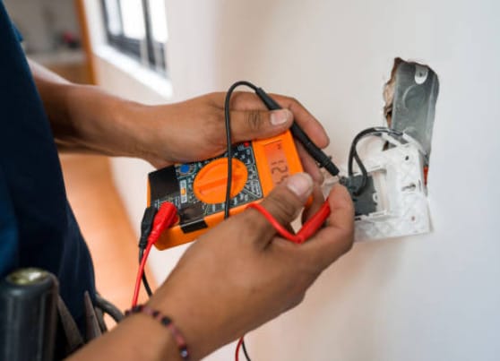 A man is working on a light switch by testing it with multimeter