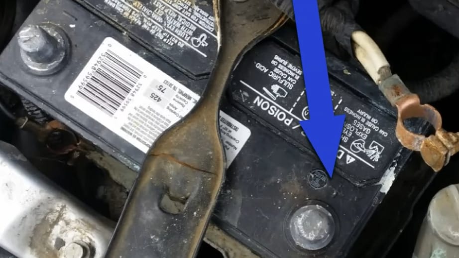 A blue arrow pointing to a battery in a car, indicating the location of the positive terminal