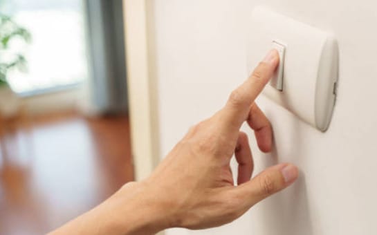 A hand is pointing at a light switch in a room