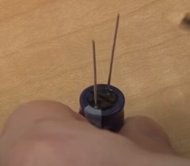 A person is holding a capacitor placed on a wooden table