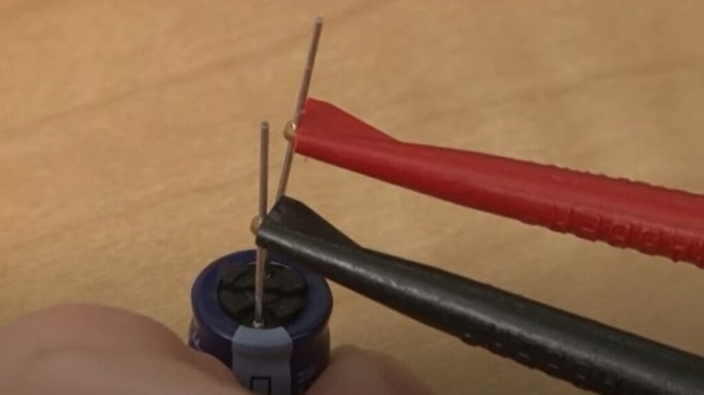 A person connecting the multimeter probe into the capacitor