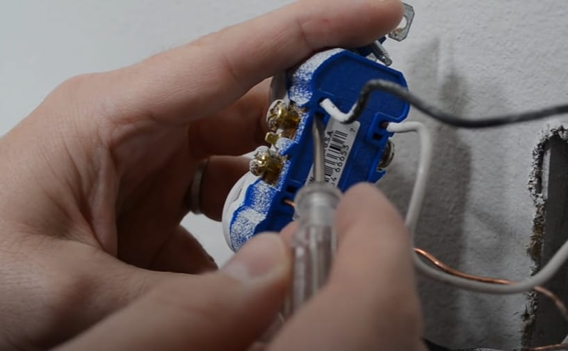 A person is securing the terminal of an outlet using a screwdriver