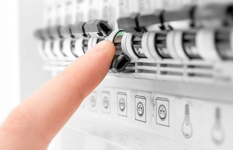A person's hand is pointing at an electrical panel