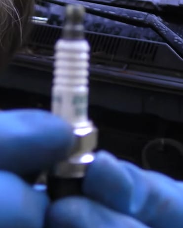 A person with blue gloves holding a car's spark plug