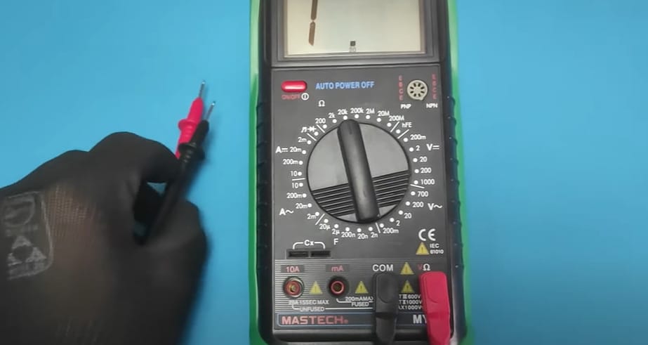 A person in black gloves holding a multimeter set in a blue background