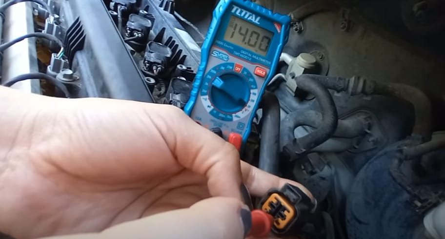 A person using a multimeter to test the O2 sensor on a car engine