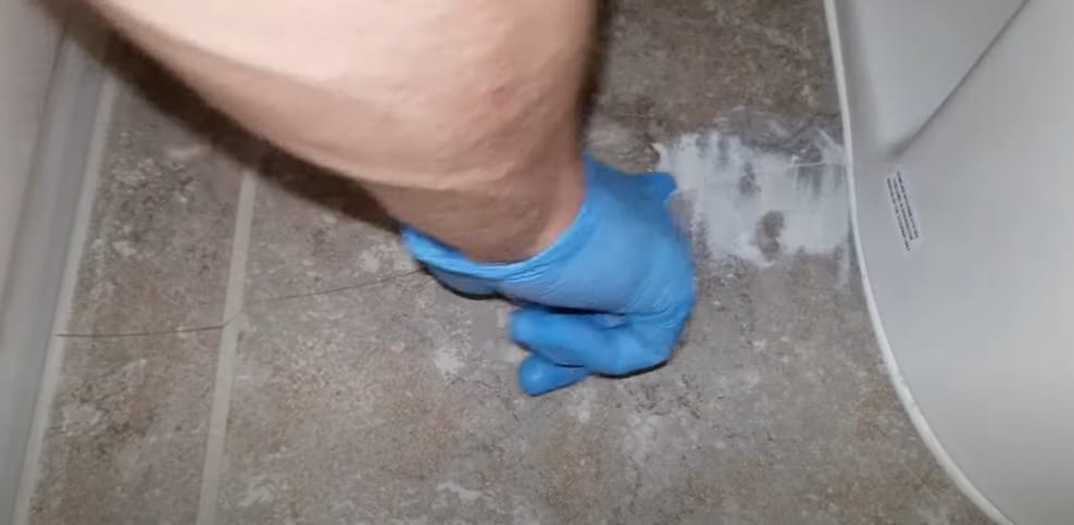 A person with blue gloves on his hand putting a mixture on the crack tile