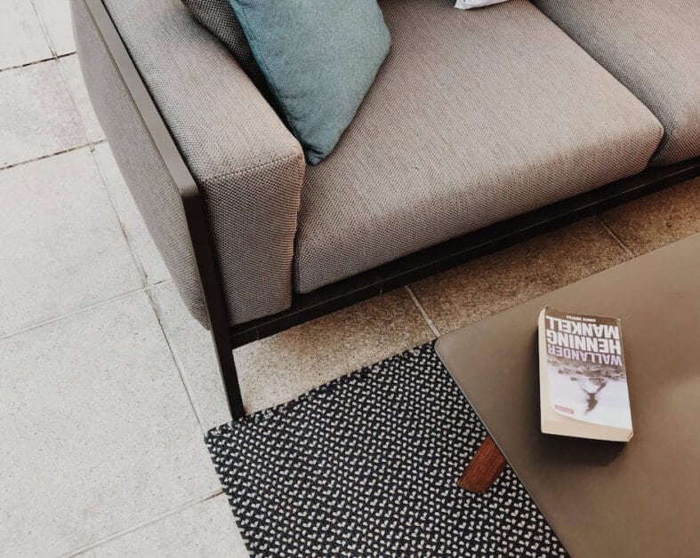 A top shot image of a couch, table, book at the top of the table, and a carpeted tiled floor