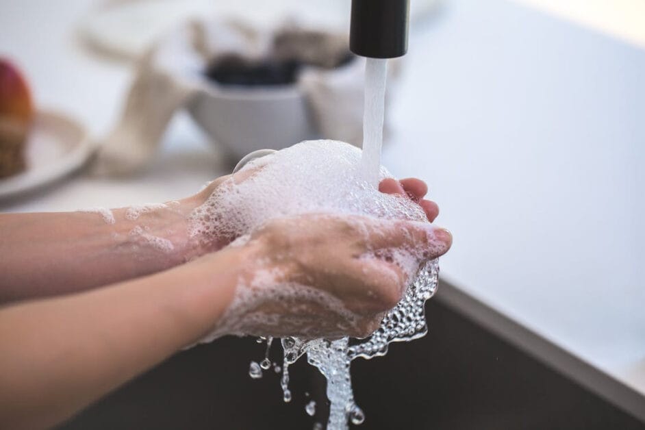 A man washing his hands with soap and running water at the kitchen faucet