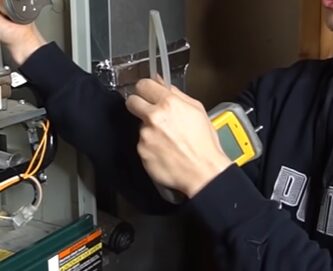 A man is working on a furnace, testing a pressure switch