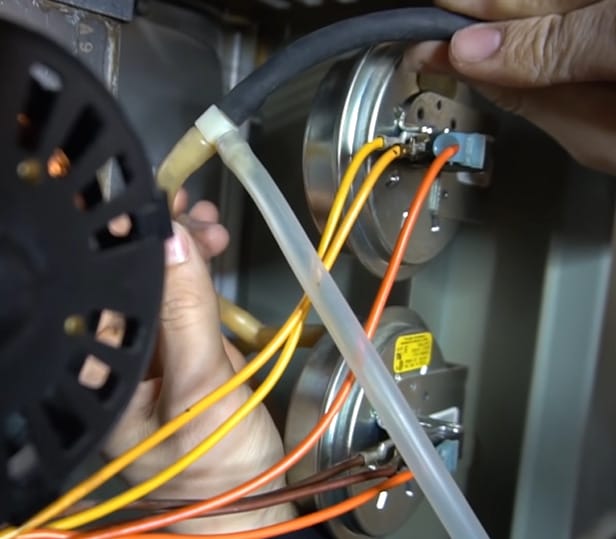 A person is working on a furnace with wires attached to it, learning how to test a pressure switch