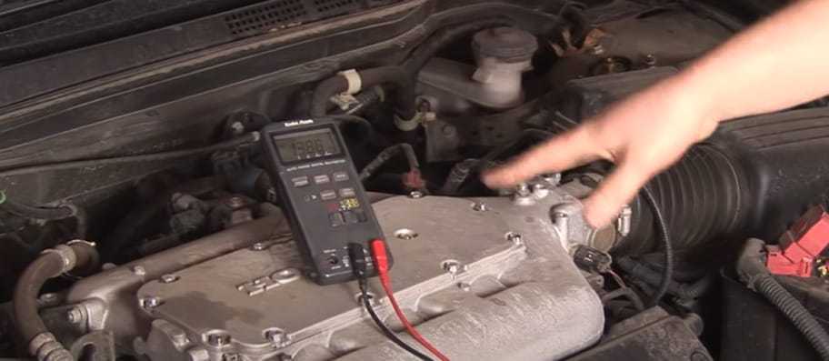 A person is pointing at the multimeter that is being used to test the engine of a car