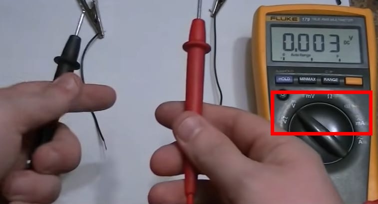 A person is holding the black and red multimeter probes