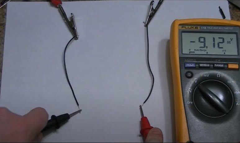 A person is testing the wires with a multimeter reading at -9.12V