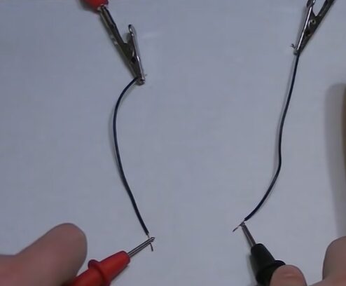 A pair of hands holding the red and black multimeter probes and testing wires