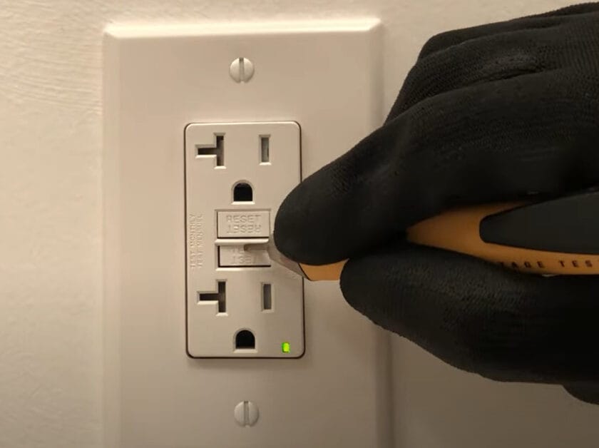 A person in black gloves is testing an outlet with a non-contact voltage tester tool