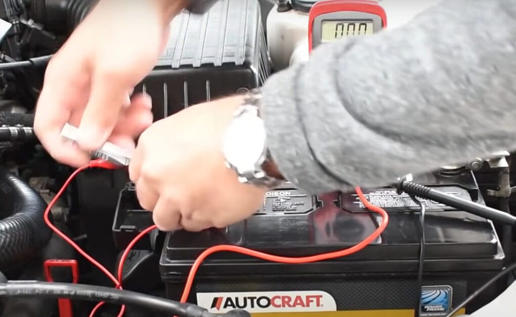 A man is using a multimeter to check for battery drain on a car