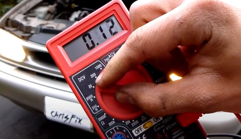 A person holding a multimeter while checking the car battery