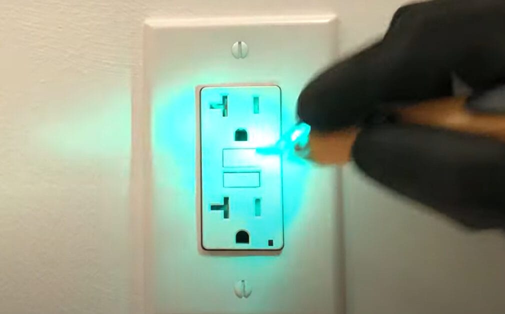 A person in black gloves checking a GFCI outlet with a non-contact voltage tester