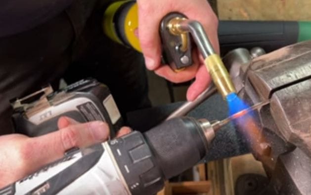 A man cutting the wire using a cordless drill and MAPP gas torch