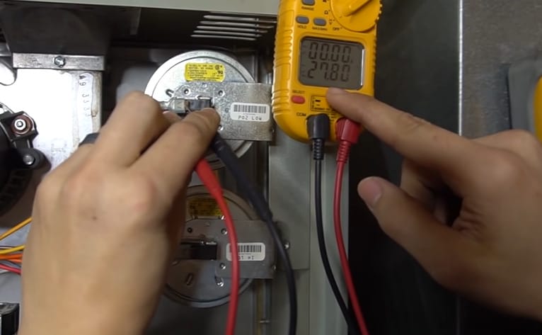A person is using a multimeter to test a heating unit and ensure the functionality of its pressure switch