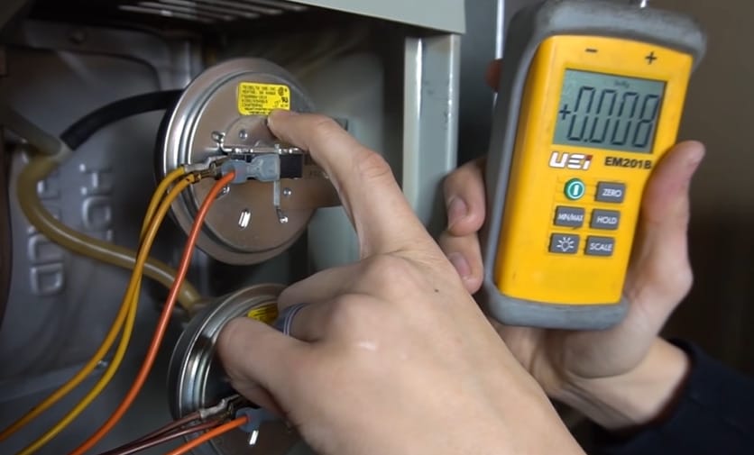 A person using a meter to test the pressure switch on a furnace