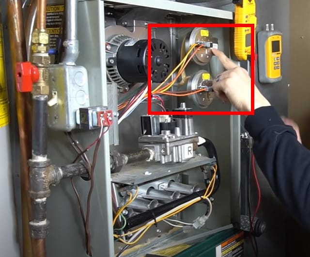 A person is demonstrating how to test the pressure switch on a gas furnace