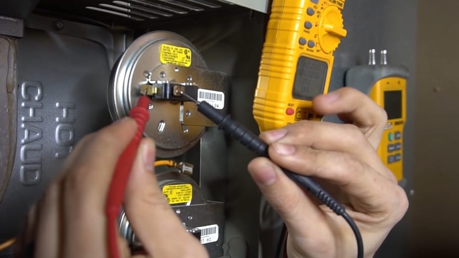 A person is working on a furnace with a wire to test a pressure switch