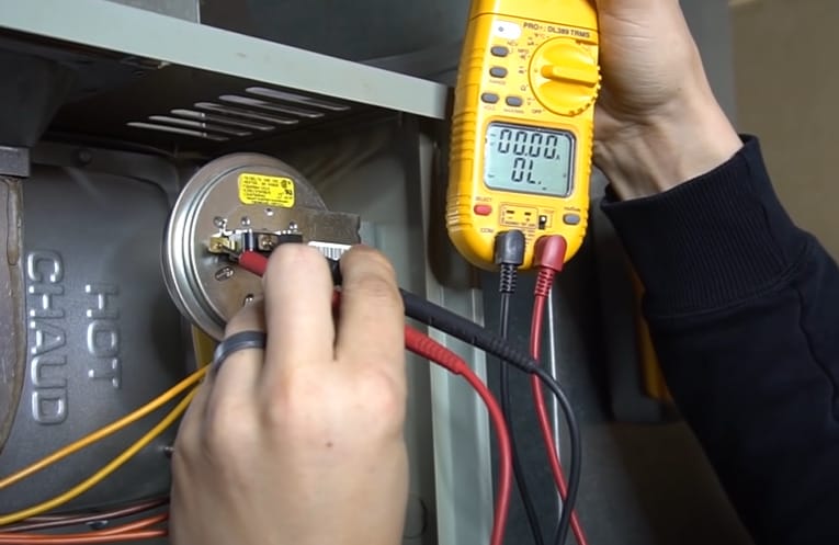 A person using a multimeter to test the wiring of an air conditioner, specifically checking the pressure switch