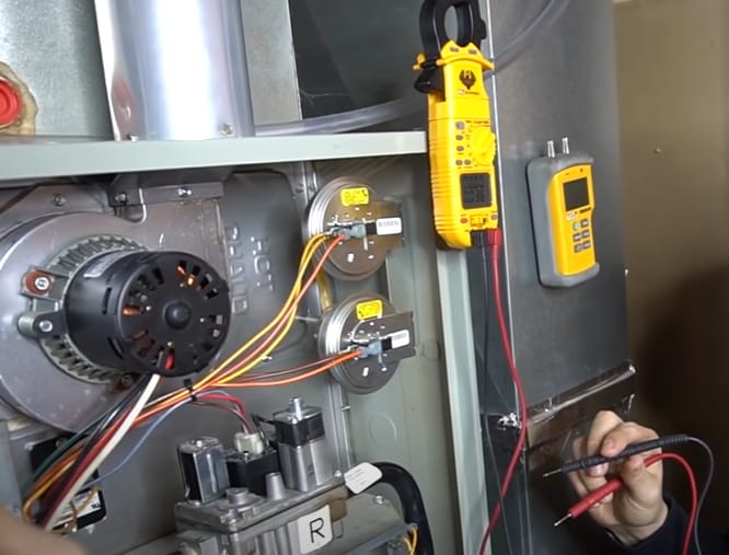 A man is working on a gas furnace, testing a pressure switch