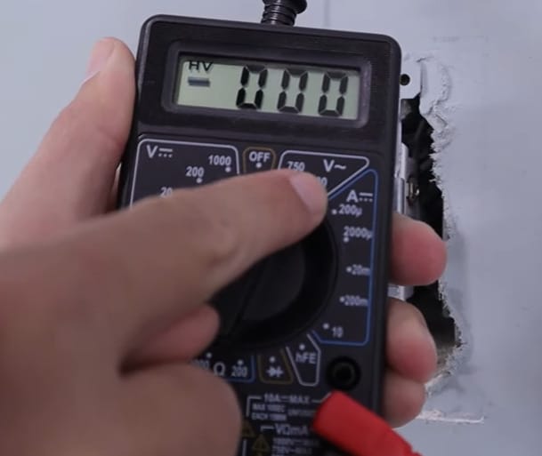A person is using a multimeter to test a wire and determine which wire is hot when both are the same color