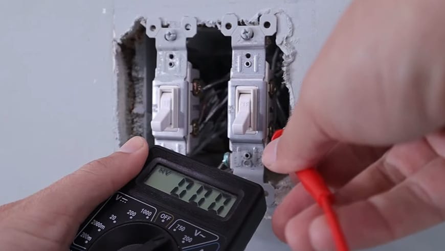 A person using a multimeter to check a light switch and determine which wire is hot when both wires are the same color
