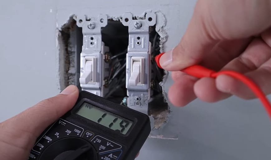 A person using a multimeter to determine which wire is hot when both are the same color